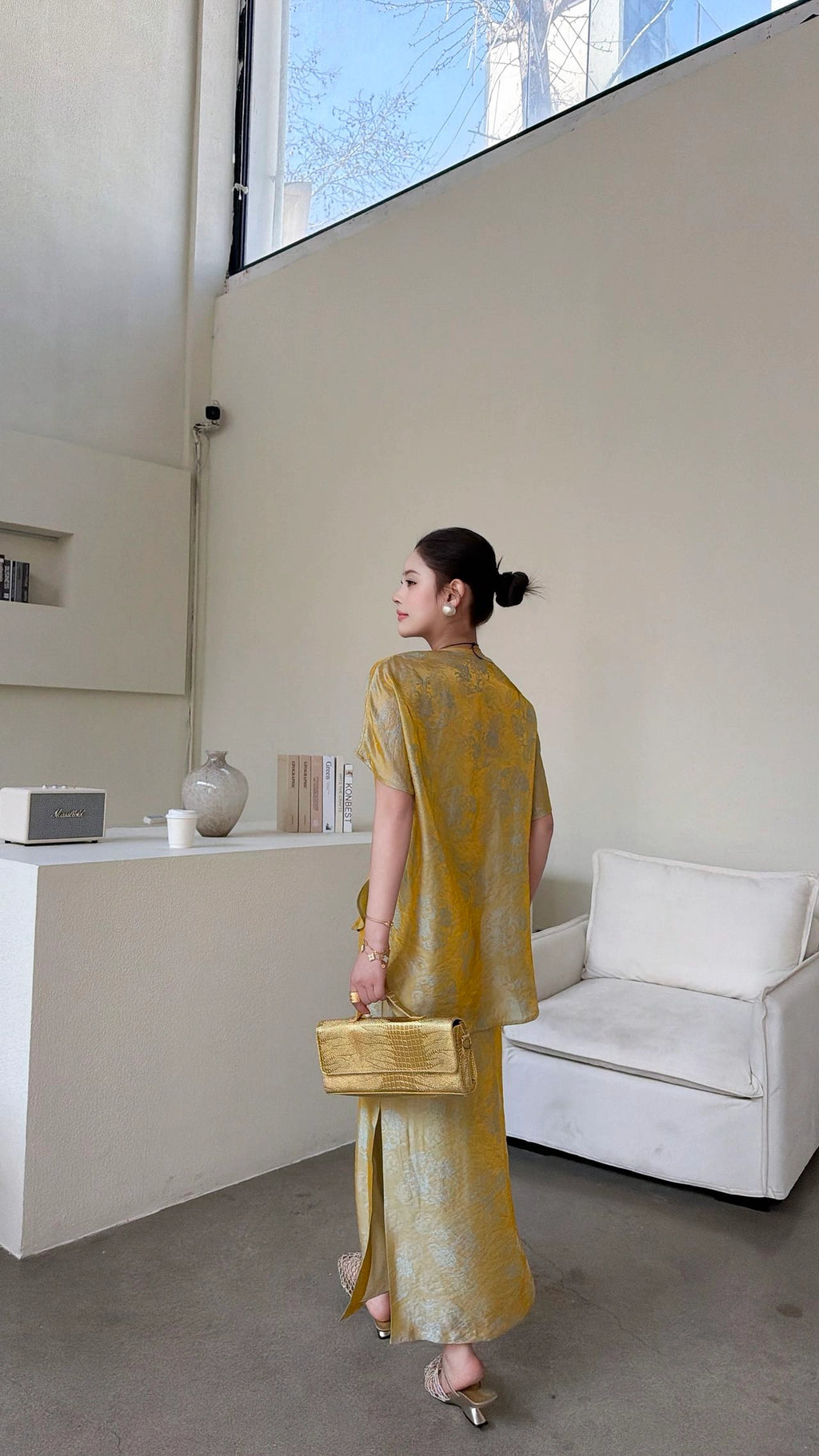 Back view of a gold Cheongsam top with short sleeves and a matching side slit maxi skirt, crafted from 80% viscose and 20% nylon, styled with a gold handbag.