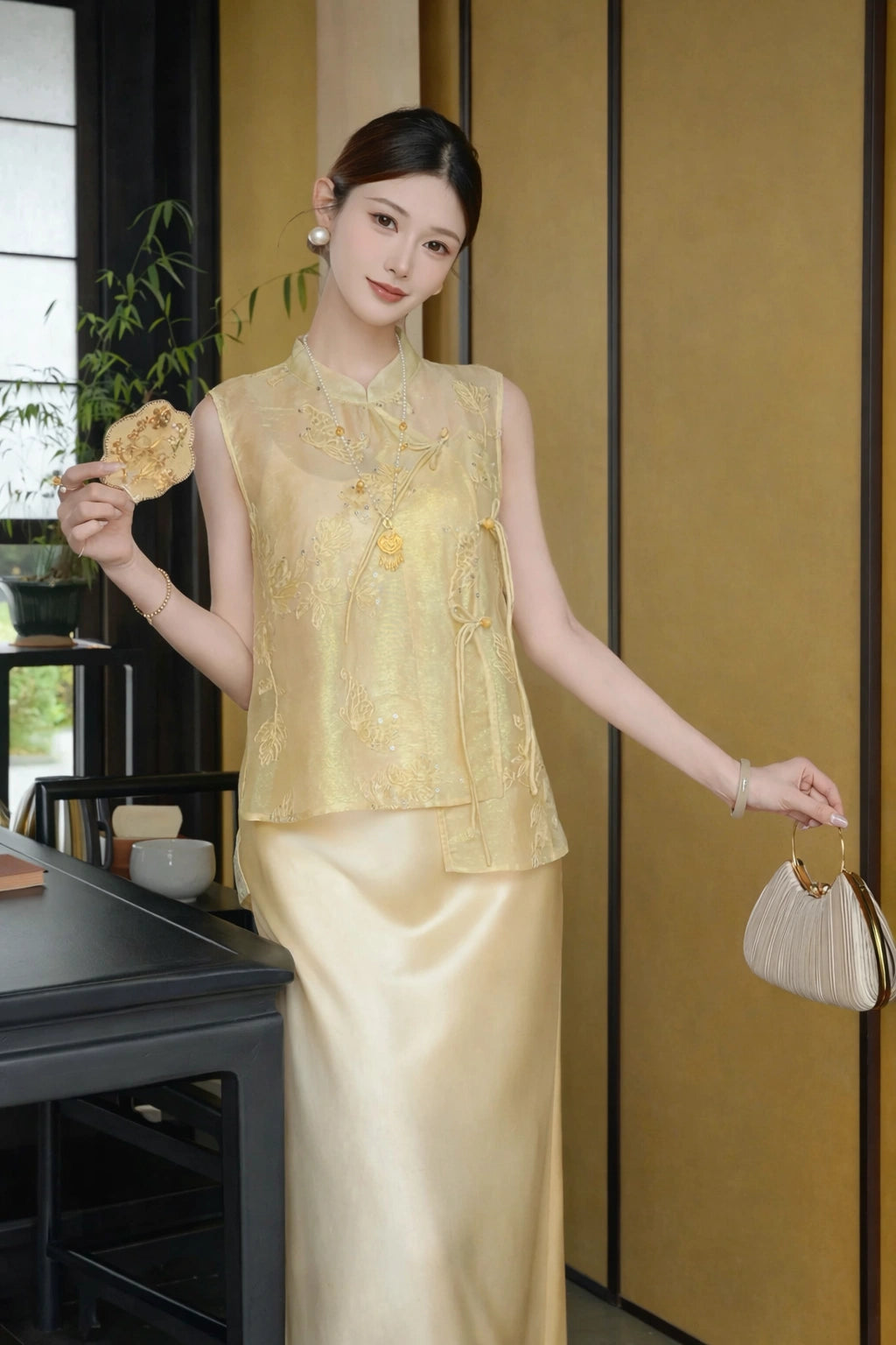 Full body shot of a gold sleeveless Cheongsam vest with floral embroidery and sequins, styled with a gold satin skirt and a handbag.