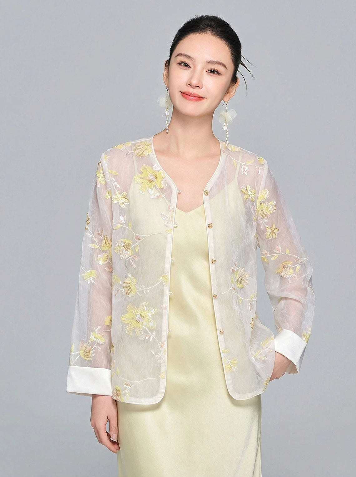 Close-up front view of a women's sheer Tencel shirt featuring delicate yellow/gold floral embroidery, sequin accents, white cuffs, and a front button closure.