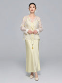 Model wearing a sheer V-neck New Chinese style shirt with intricate yellow/gold floral embroidery and sequins, paired with a matching satin skirt, holding a long pearl necklace.