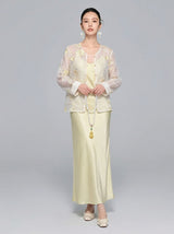 Model wearing a sheer V-neck New Chinese style shirt with intricate yellow/gold floral embroidery and sequins, paired with a matching satin skirt, holding a long pearl necklace.