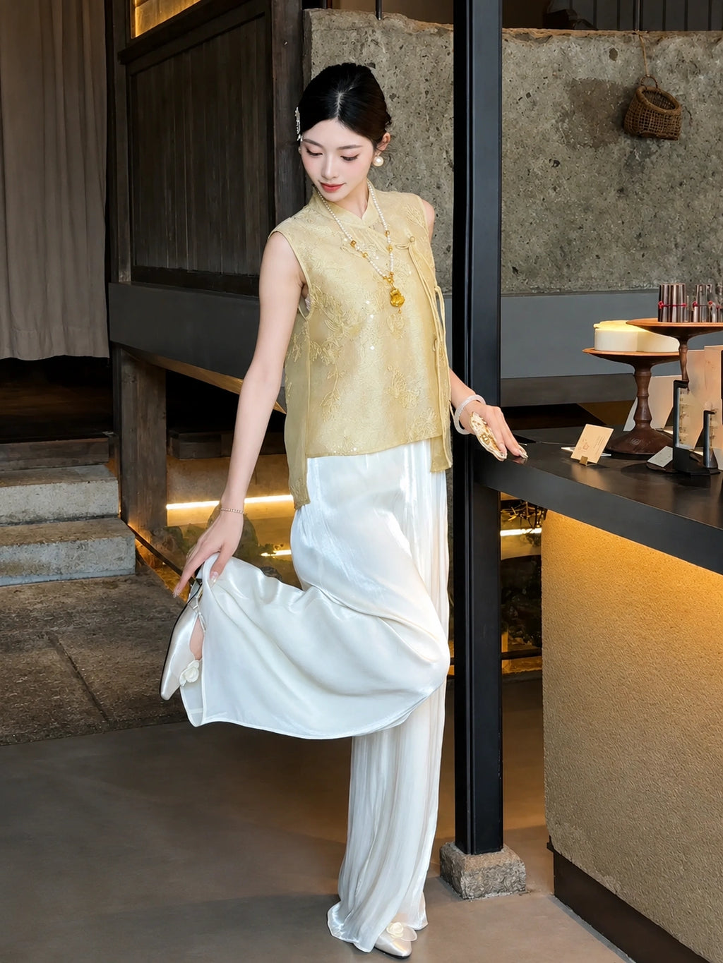 Side view of a gold Cheongsam top worn with white wide-leg palazzo pants, styled with a fan and pearl necklace.