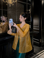 Close lifestyle view of a golden amber silk cardigan highlighting the sheer texture and frog-button front.