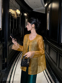 Woman wearing a golden amber pure silk sheer cardigan with traditional frog-button closures over an emerald green dress.