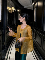 Woman wearing a golden amber pure silk sheer cardigan with traditional frog-button closures over an emerald green dress.