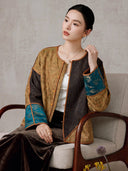 Seated model wearing the gold and dark-brown colorblock jacket with teal patterned cuffs
