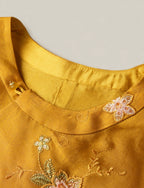 Close-up detail of golden mulberry silk vest featuring floral embroidery and Chinese knot button design