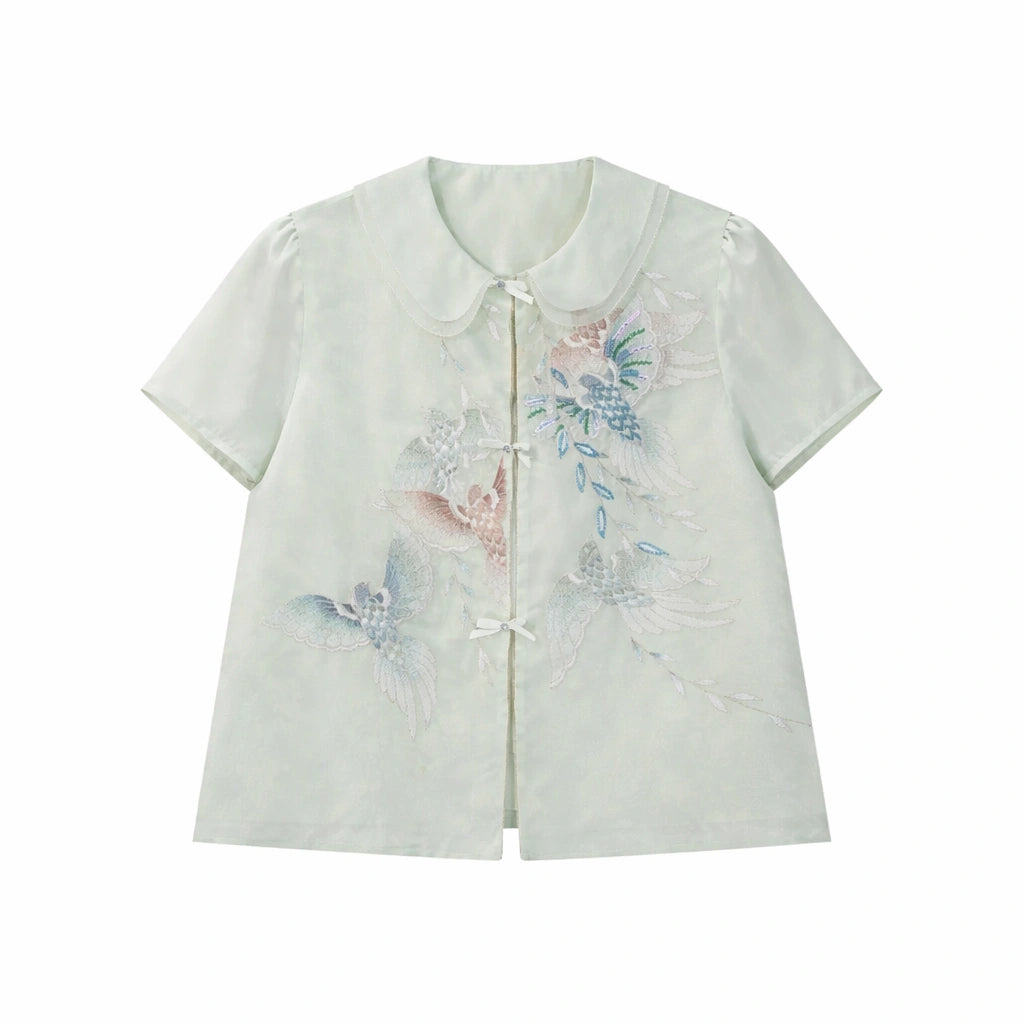 Flat lay of a light green short-sleeve top with a Peter Pan collar and delicate butterfly & floral embroidery, featuring a front button closure.