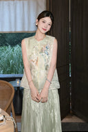 Model wearing a light green sleeveless vest with a Peter Pan collar, intricate butterfly and floral embroidery, and a front button closure, paired with a pleated skirt.