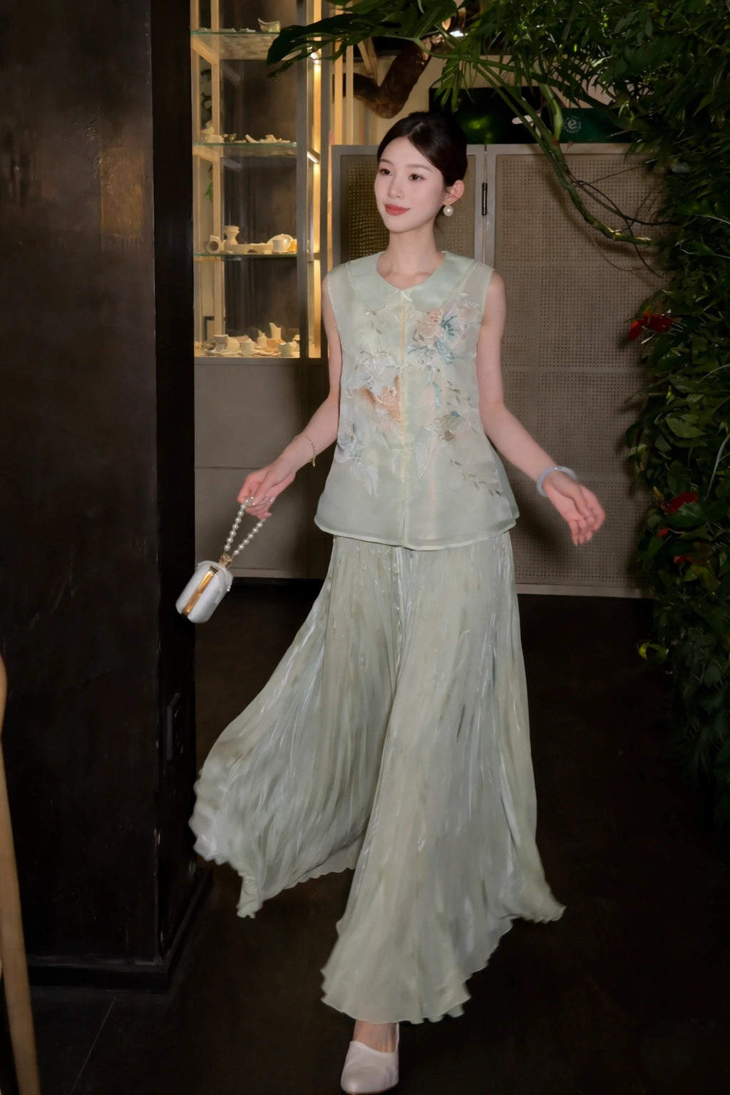 Full body shot of a green sleeveless embroidered top paired with a matching pleated skirt, holding a white handbag, perfect for a New Chinese style look.