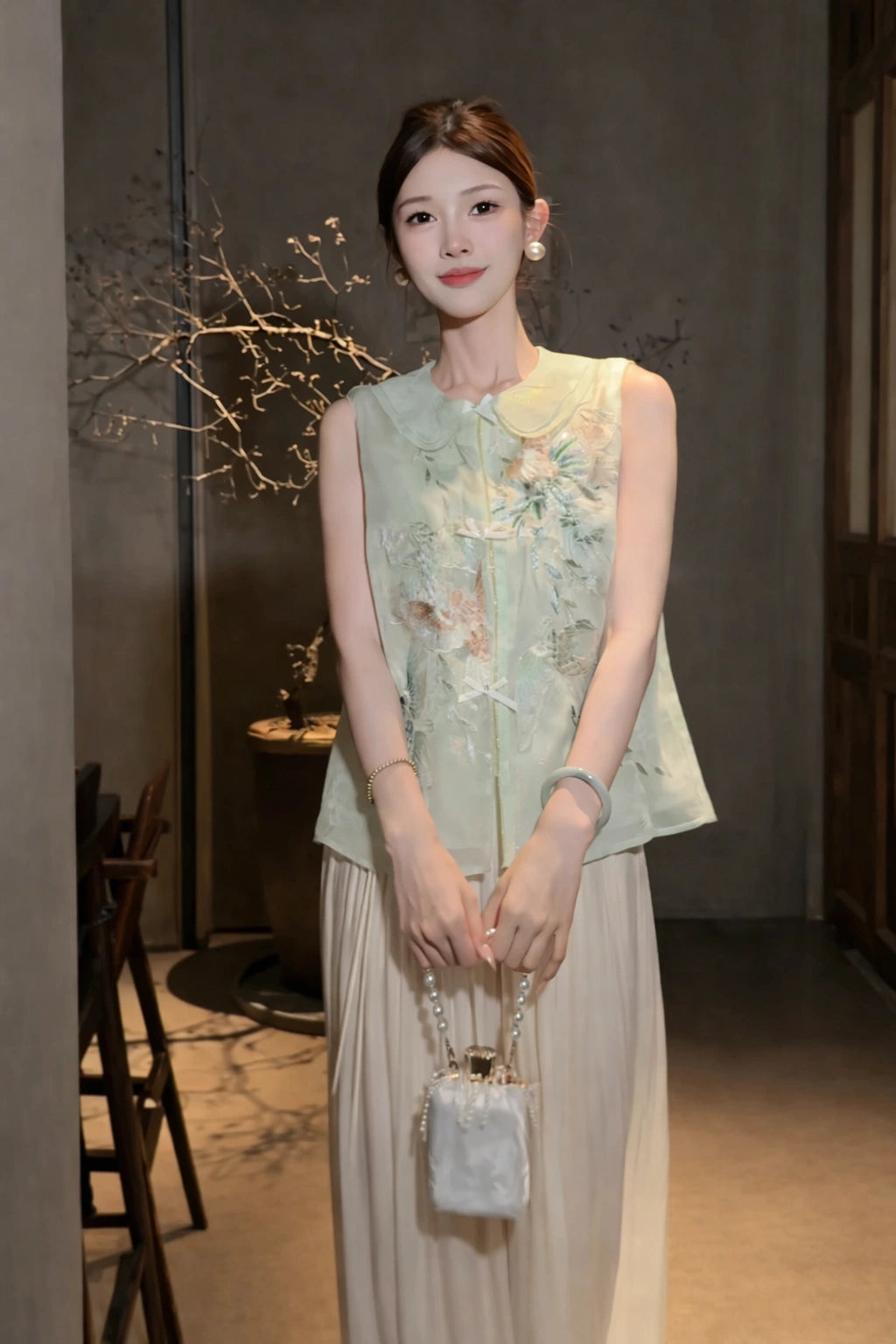 Model wearing a green sleeveless Cheongsam-style vest with floral embroidery and a Peter Pan collar, styled with white wide-leg trousers and a pearl bag.