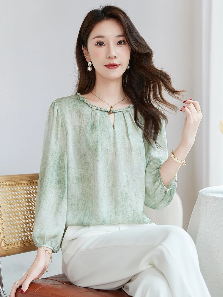Model wearing a mint green 100% silk blouse with a braided neckline and puff sleeves, styled with white pants and a green handbag.