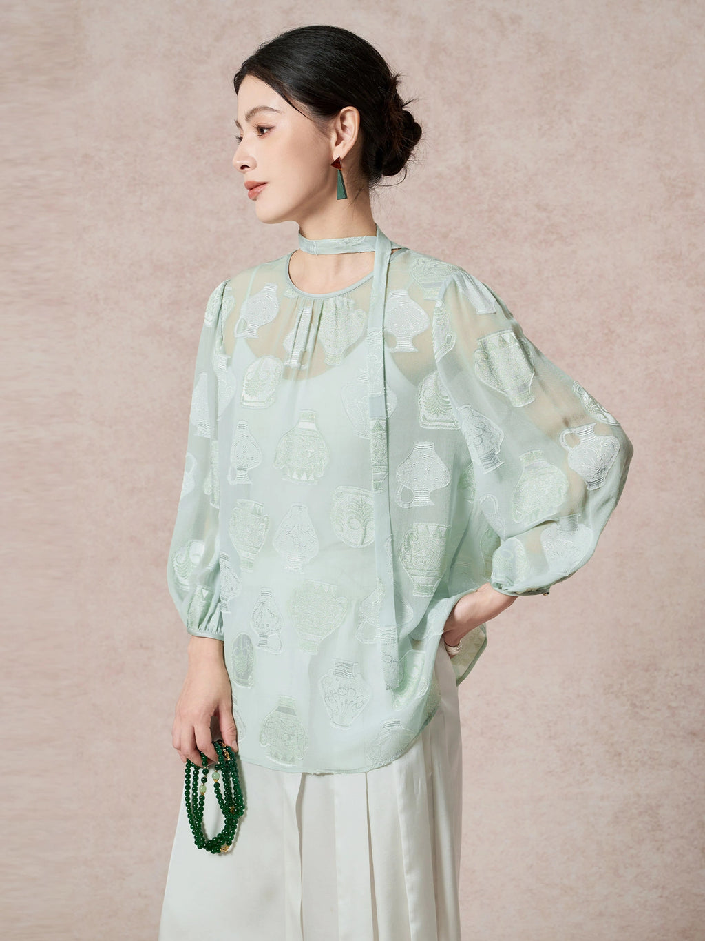 Side view of a green mulberry silk blouse featuring the sheer cutwork fabric and a relaxed, billowy sleeve silhouette.