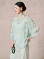 Side view of a green mulberry silk blouse featuring the sheer cutwork fabric and a relaxed, billowy sleeve silhouette.