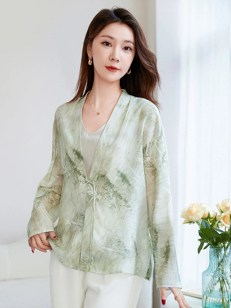Model wearing a light green 100% mulberry silk open-front shirt with a V-neck and tie closure, featuring an elegant watercolor bamboo and leaf print, paired with white trousers.