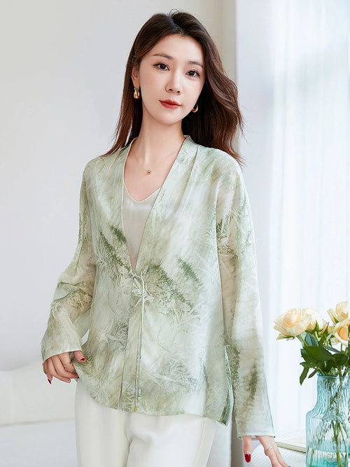 Model wearing a light green 100% mulberry silk open-front shirt with a V-neck and tie closure, featuring an elegant watercolor bamboo and leaf print, paired with white trousers.