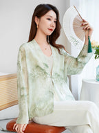 Model seated in a light green mulberry silk open-front shirt, holding a white fan, showcasing the lightweight, breathable fabric and artistic watercolor print.