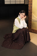 Seated styling of the green Song brocade vest with a white blouse and flowing skirt