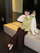 Woman seated in a green floral Song brocade vest with a curved hem