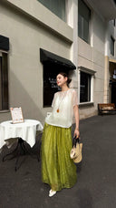 Side view of bright green wide-leg trousers with a flowy drape, crafted from a viscose-polyester blend, styled with white heels and a straw tote.