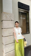 Woman wearing lime green wide-leg palazzo pants with a relaxed fit, paired with a sheer white short sleeve top and a straw bag.