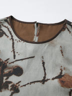 Close-up of the back neckline of a grey silk tank top featuring a hidden zipper, brown trim, and the intricate ink wash print texture.