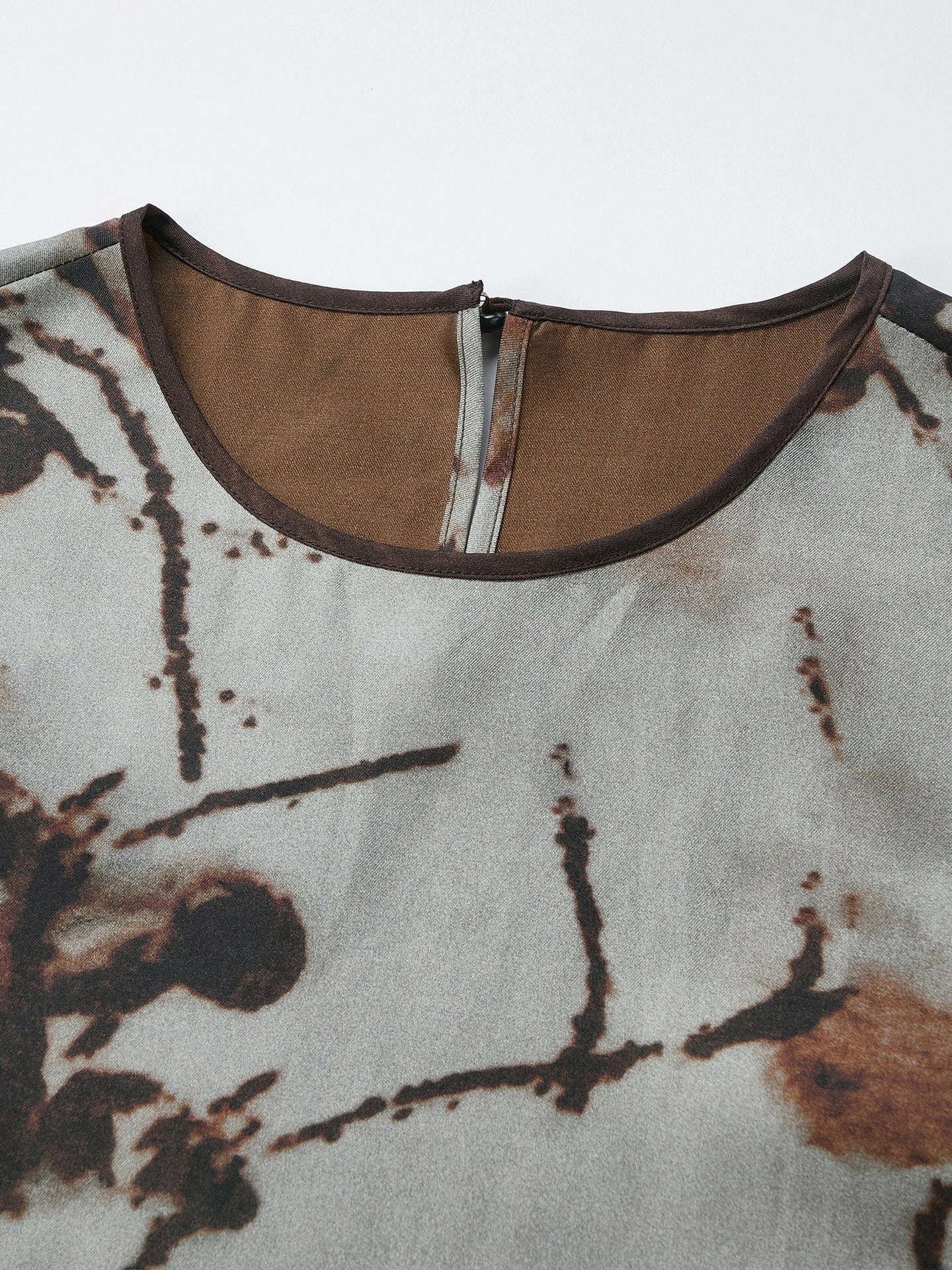 Close-up of the back neckline of a grey silk tank top featuring a hidden zipper, brown trim, and the intricate ink wash print texture.