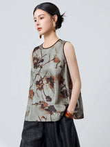 Side profile of a women's grey silk tank top with brown piping and an abstract floral pattern, styled with black pants and a brown bag.