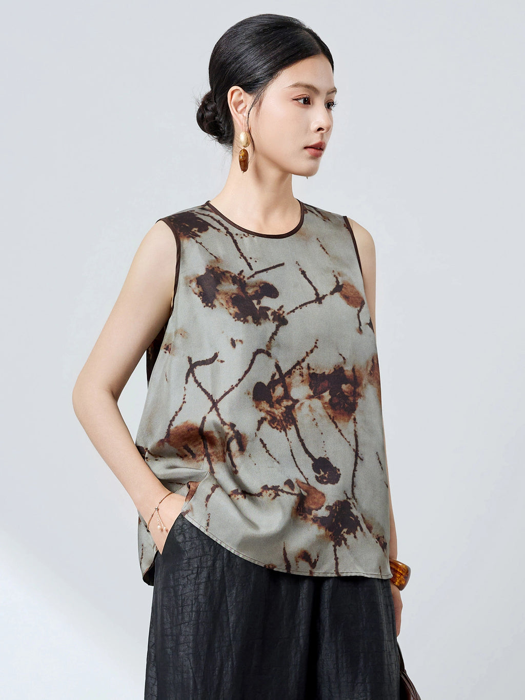 Side view of a grey 100% mulberry silk tank top with a relaxed A-line silhouette and burnt-umber ink pattern, paired with black textured pants.