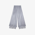 Flat lay of grey pleated wide-leg pants with an elastic waistband, side tie, and layered lace hem, crafted from 100% polyester.