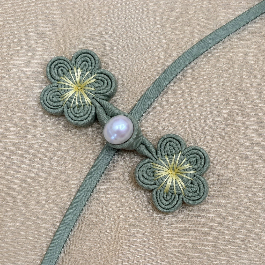 Close-up of handmade sage green plum blossom frog buttons with a pearl-style accent