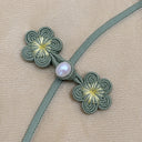 Close-up of handmade sage green plum blossom frog buttons with a pearl-style accent
