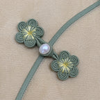 Close-up of handmade sage green plum blossom frog buttons with a pearl-style accent