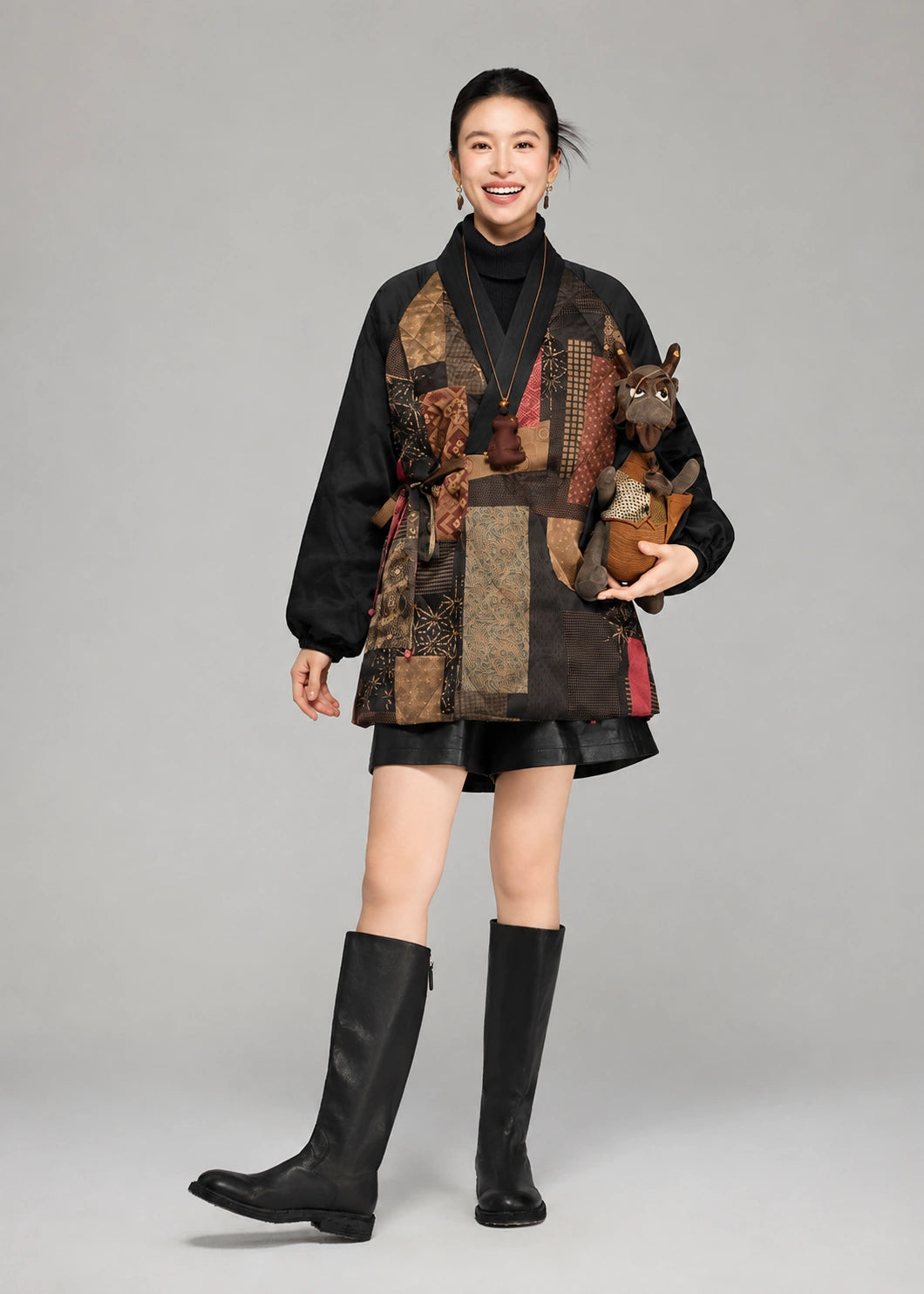 Woman wearing a black Gambiered Silk goose down coat with multicolor patchwork motifs and a wrap waist tie.