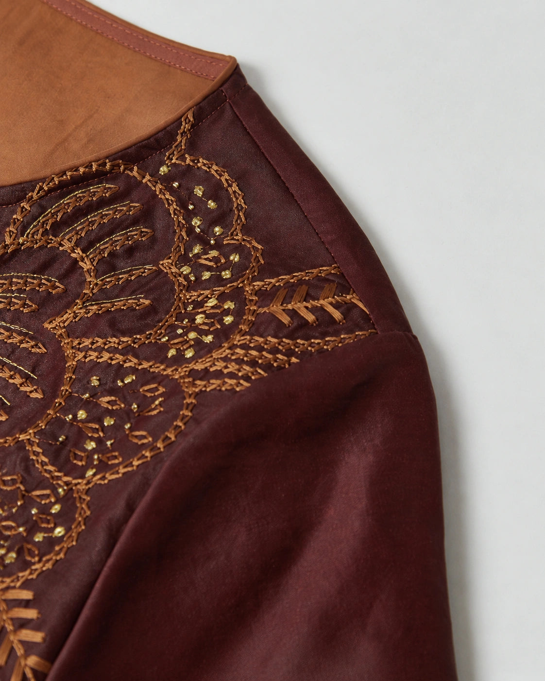 Detailed view of the amber and gold botanical embroidery on the wine-red mulberry silk dress