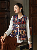 Model seated in an open Inkstone Blue embroidered vest over a white blouse