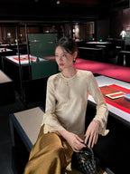 Elegant ivory acetate jacquard long sleeve blouse paired with a satin skirt in a refined dining setting.