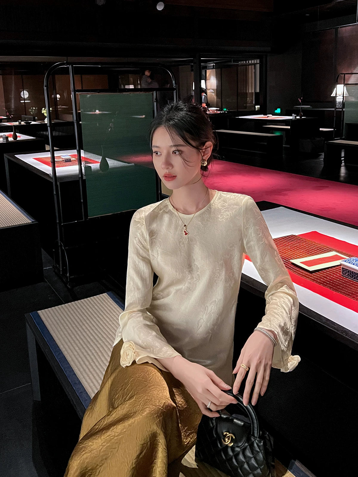 Elegant ivory acetate jacquard long sleeve blouse paired with a satin skirt in a refined dining setting.