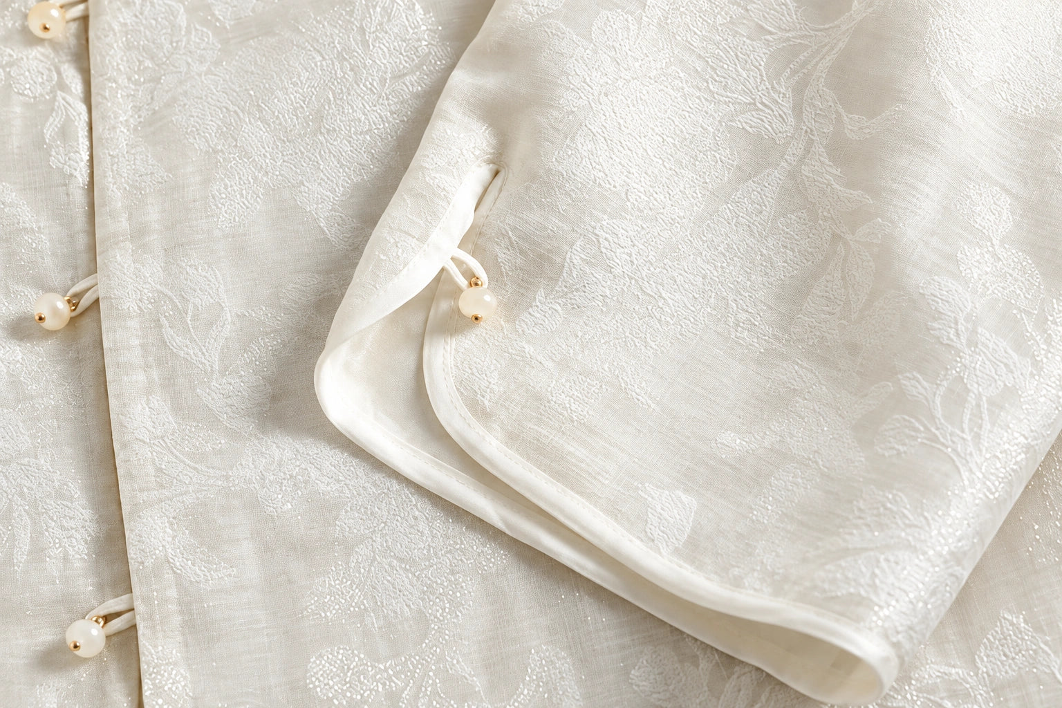 Close-up of the Ivory jacquard jacket showing its curved cuff edge, narrow white edging and button-and-loop fastenings