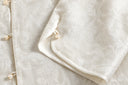 Close-up of a curved split cuff with an ivory button and loop, showing the jacket’s shimmering floral jacquard.
