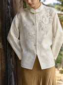 Close view of an ivory jacket showing layered sequin flowers, beaded leaves, a decorated stand collar and front buttons.