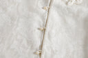 Close-up of tonal floral jacquard with a subtle shimmer and rounded ivory buttons attached to fabric loops.