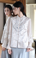 Model beside a mirror wearing the ivory vest with blue scroll embroidery and front buttons.