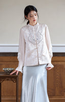 Model wearing an ivory jacquard vest with blue chest embroidery, layered over a long-sleeve top and satin skirt.