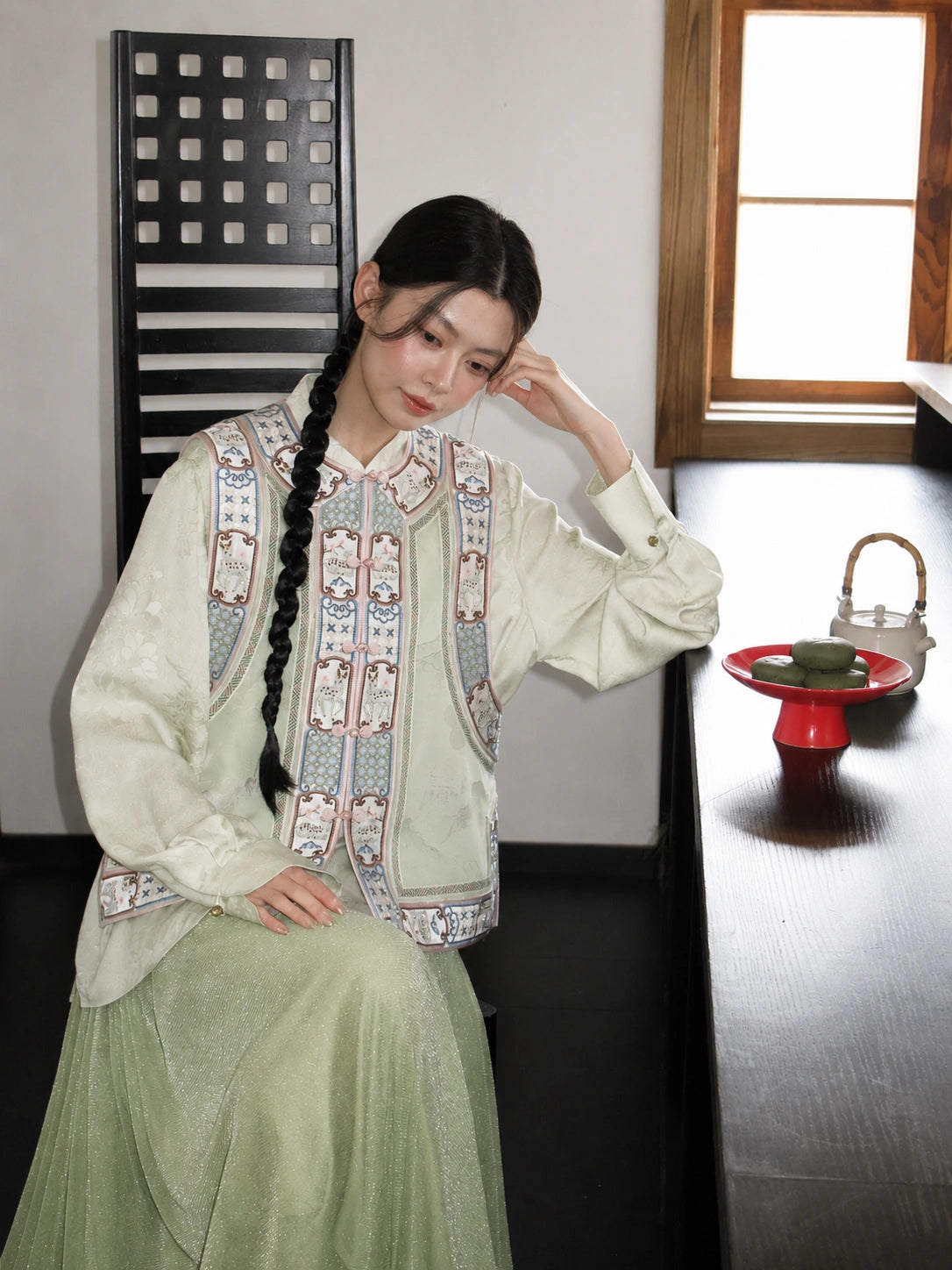 Seated model wearing an ivory floral Chinese-style silk vest with a refined traditional silhouette.