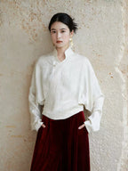 Woman wearing an ivory Mandarin collar wrap blouse with a burgundy velvet skirt.