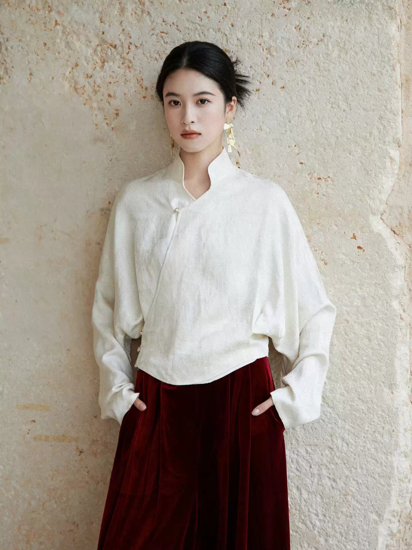 Woman wearing an ivory Mandarin collar wrap blouse with a burgundy velvet skirt.