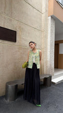 Front view of a New Chinese style vest top featuring a Mandarin collar and traditional frog closures, styled with black flowy trousers and a green shoulder bag.