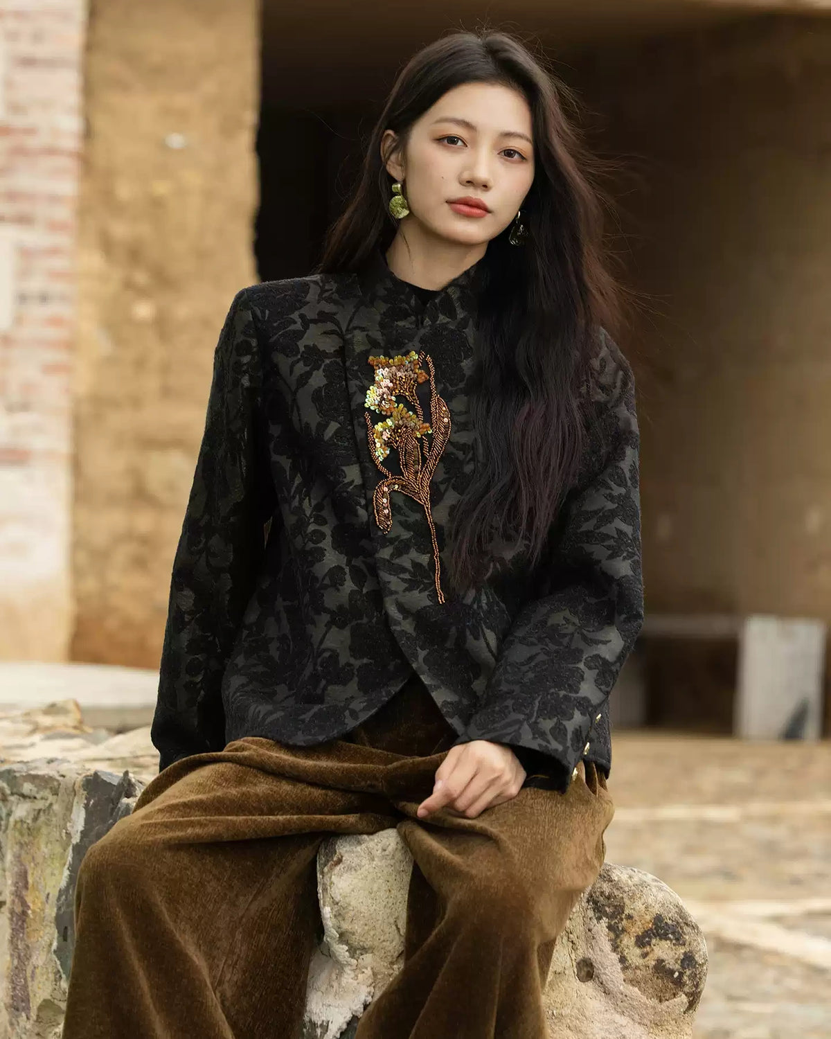 Seated model wearing the Jianwu stand-collar jacket with a floral appliqué and curved front corners