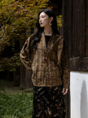 Model wearing the buttoned Mingcha Brown plaid jacket beside a dark wooden wall.